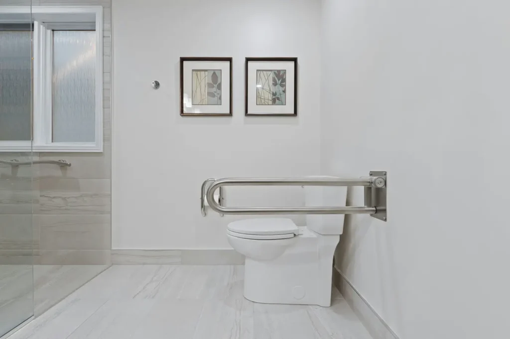 Bathroom with a stainless steel grab bar beside the toilet and a curbless walk-in shower entry