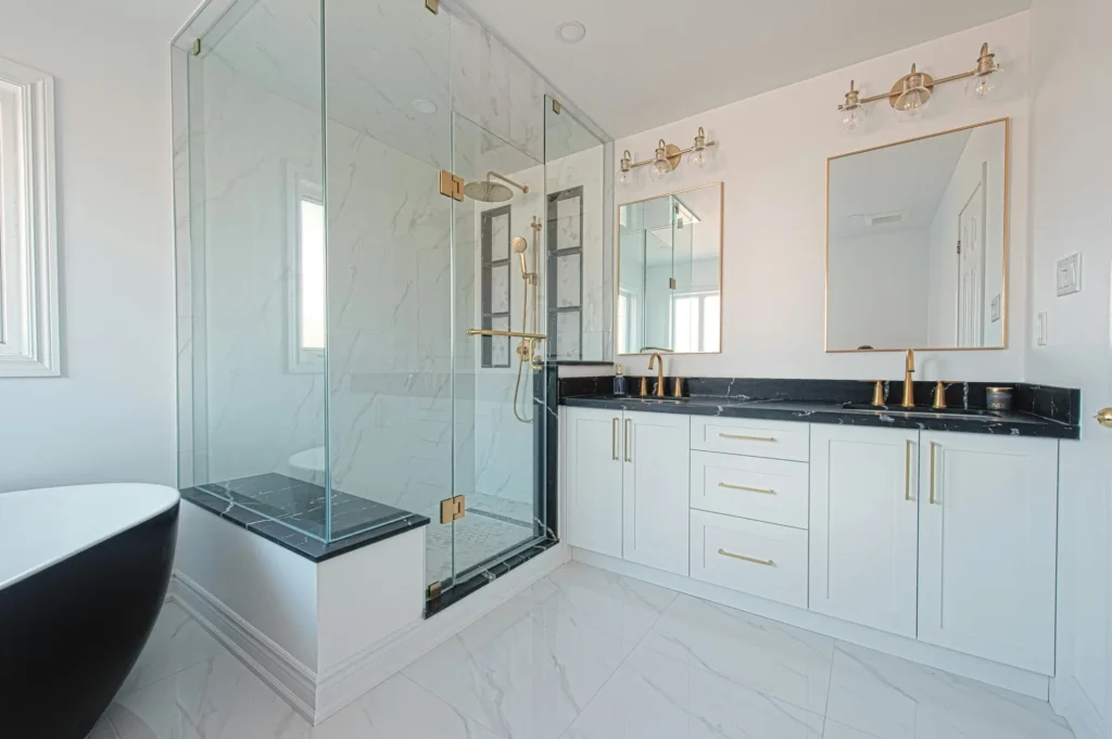 Porcelain and natural stone tile bathroom in Burlington with large-format marble-look shower walls, glass enclosure, and black freestanding tub