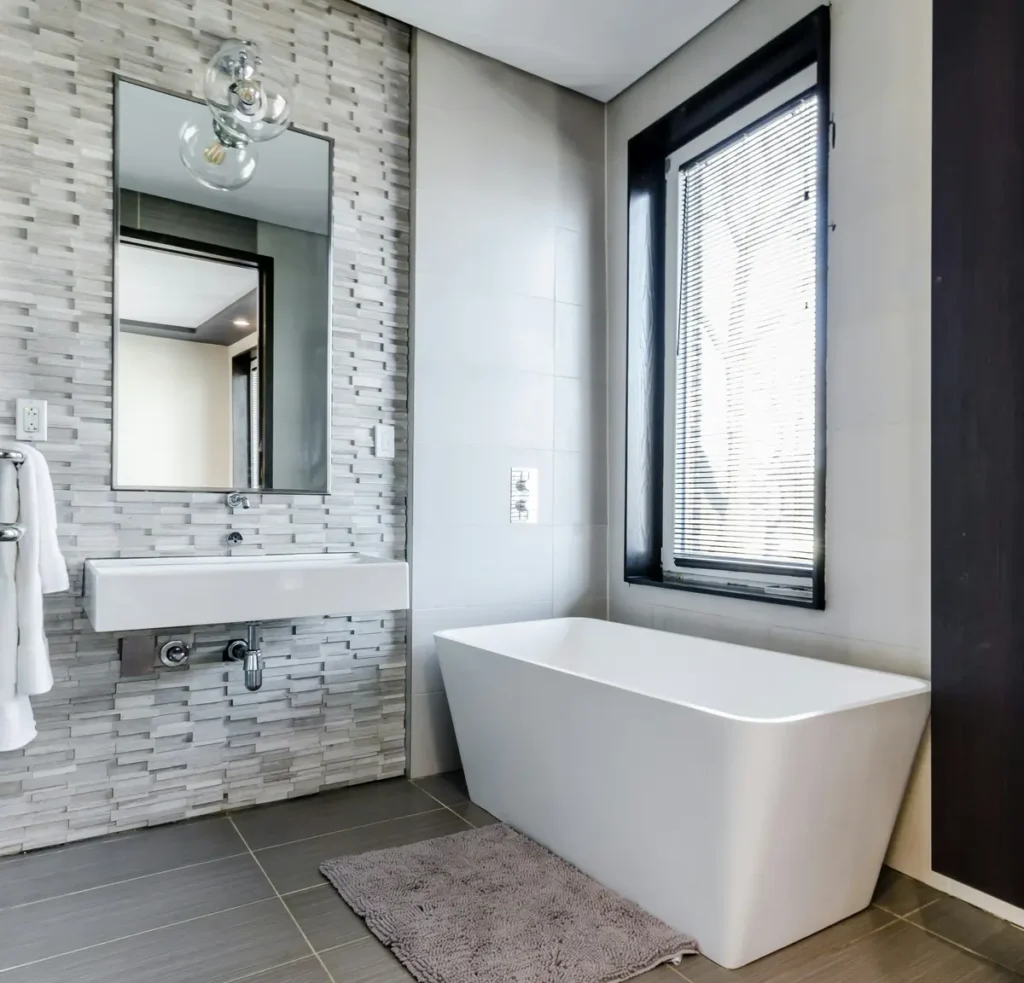 Textured stacked stone tile accent wall behind a wall-mounted sink, with a freestanding tub and dark tile flooring