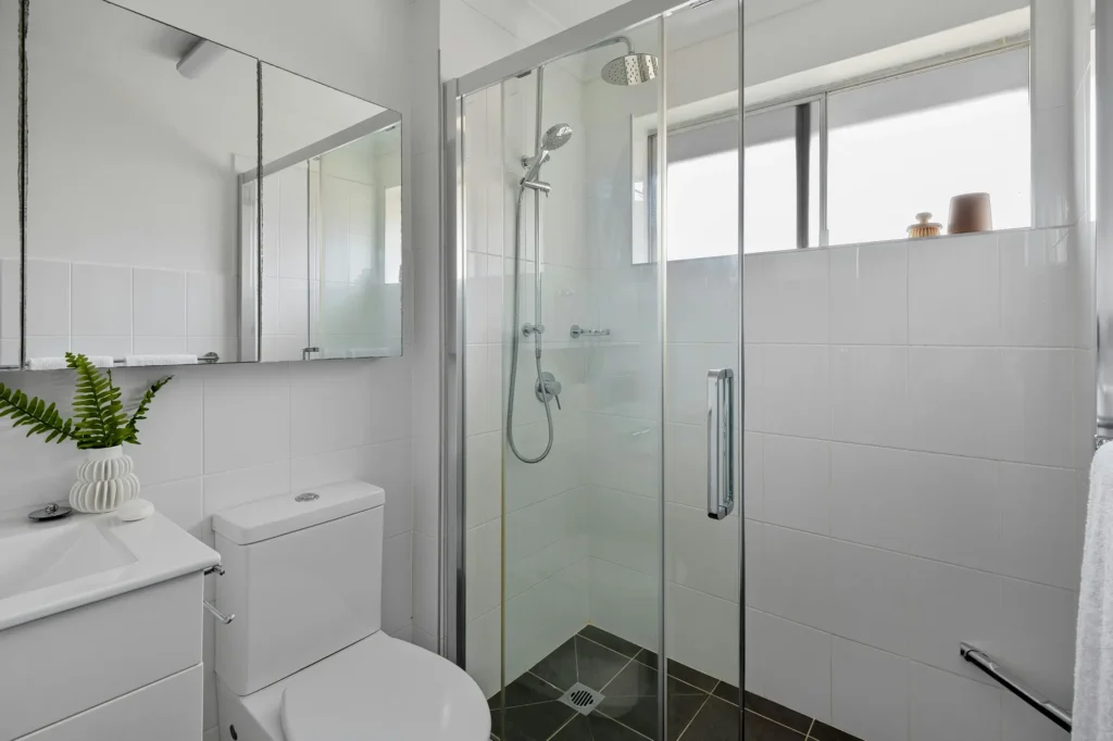Corner glass shower enclosure with rain showerhead, handheld shower, and dark tile flooring in a Roseland, Burlington bathroom