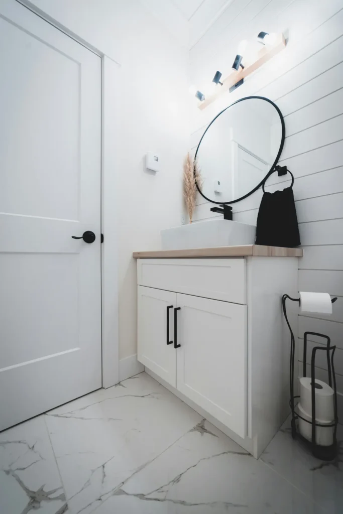 White shaker-style bathroom vanity with wood-look countertop, vessel sink, and round black mirror in an Alton Village, Burlington bathroom