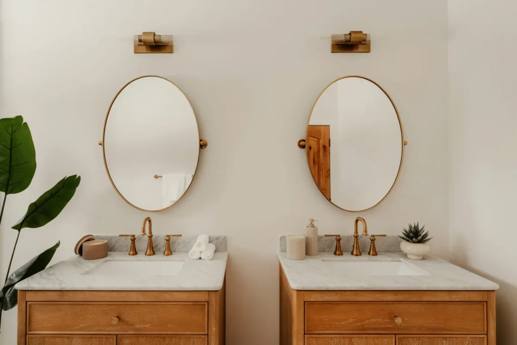 Custom double bathroom vanity with wood cabinetry, marble countertop, oval mirrors, and brass fixtures