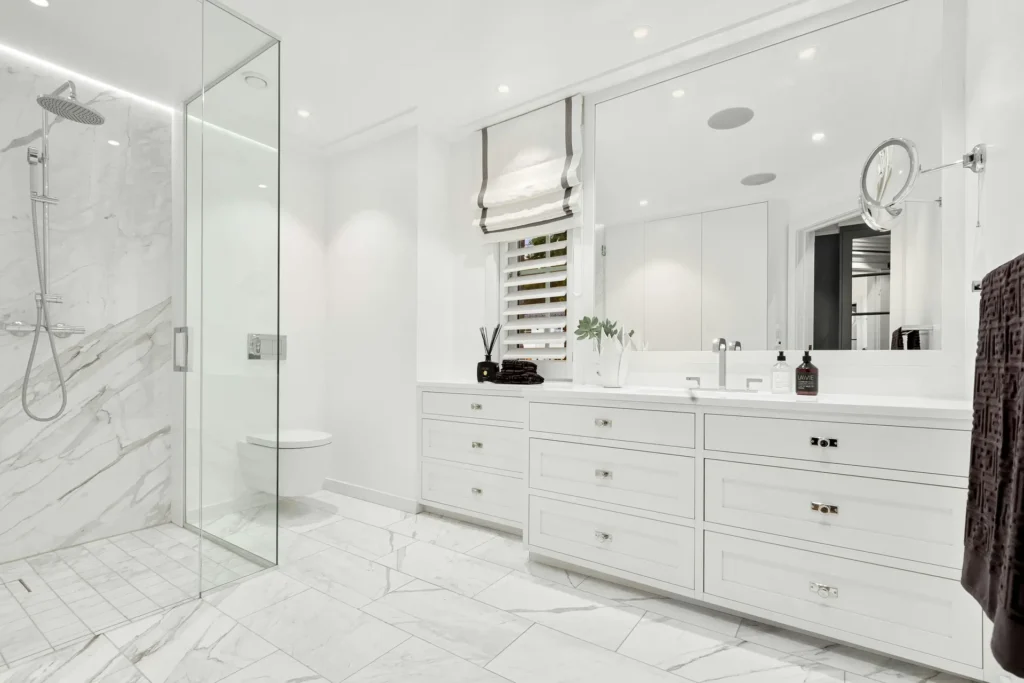 Custom white bathroom vanity and cabinetry with marble countertop, framed mirror, and glass shower in a Roseland, Burlington bathroom