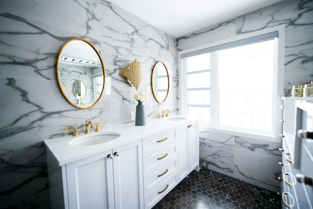 Double sink luxury bathroom vanity with marble walls and gold fixtures in Burlington