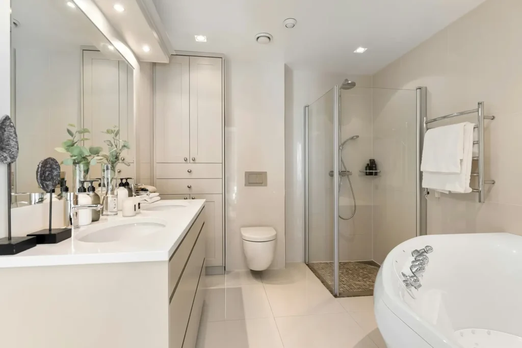 Modern full bathroom renovation with a cream double vanity, tall storage cabinetry, glass shower, and freestanding tub