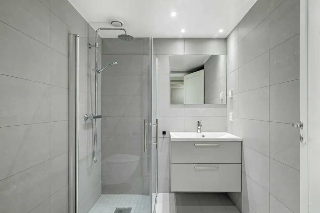 Burlington bathroom with glass shower door and chrome hardware, rainfall showerhead, tile walls, floor drain, vanity, and mirror