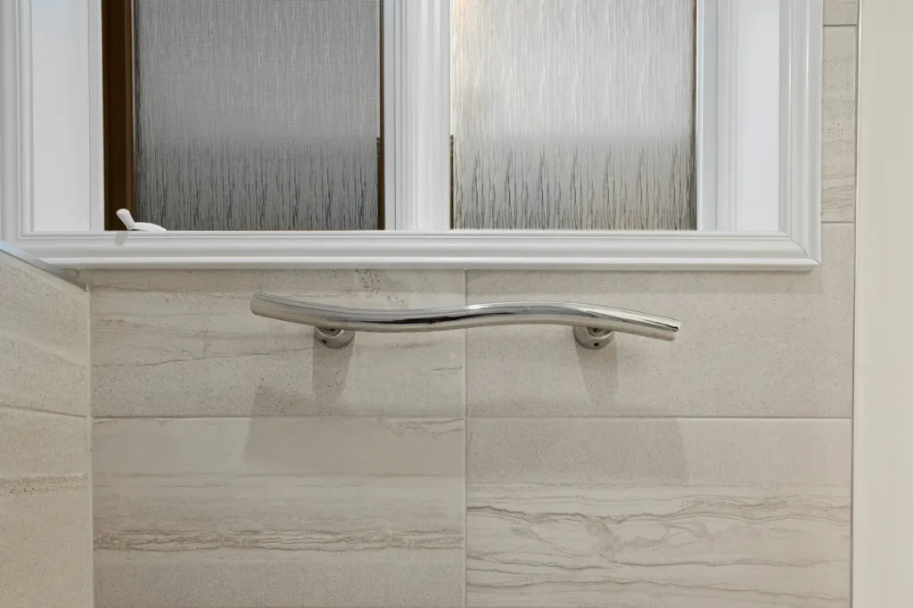 grab bar installed on a tiled bathroom wall beneath a frosted glass window in an accessible Burlington bathroom