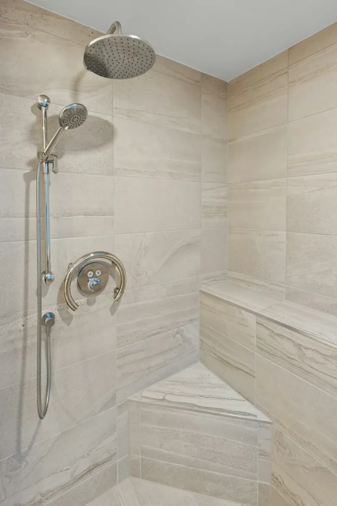 Tiled walk-in shower in an accessible Burlington bathroom with a rain shower head, handheld showerhead, and built-in corner bench seat