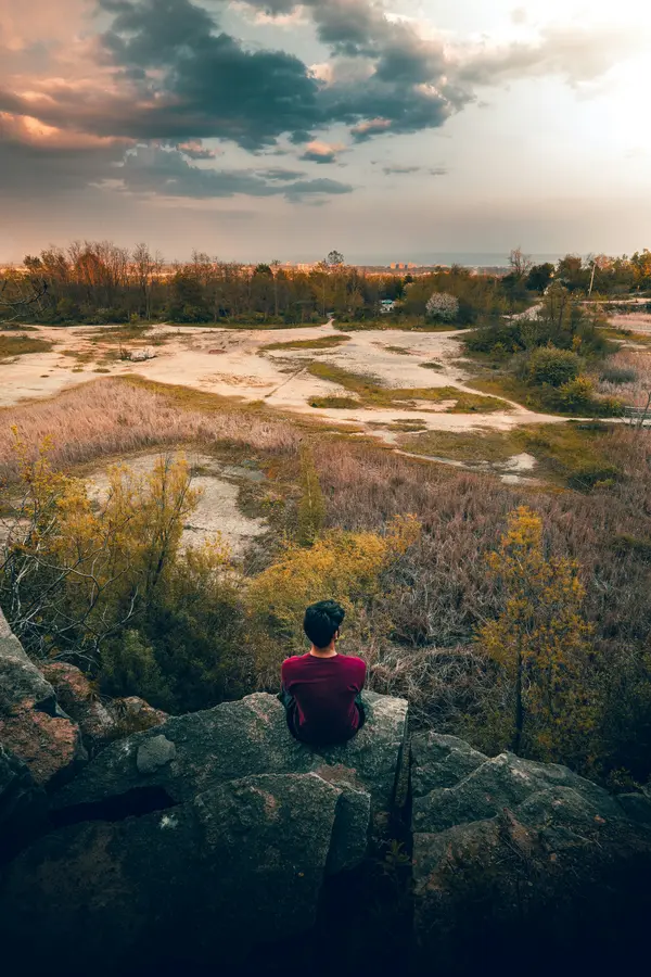 Person sitting on a rock overlooking the autumn escarpment landscape at Kerncliff Park, Burlington, Ontario
