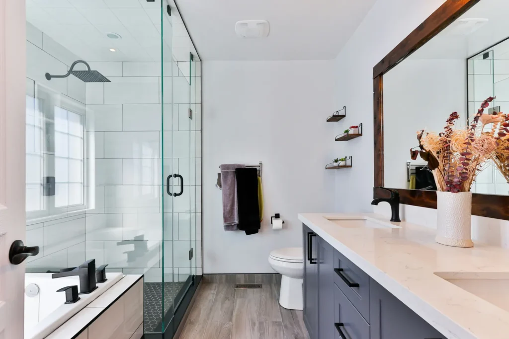 Modern Burlington bathroom with glass shower enclosure, black matte fixtures, wood-look flooring, floating shelves, and vanity with mirror