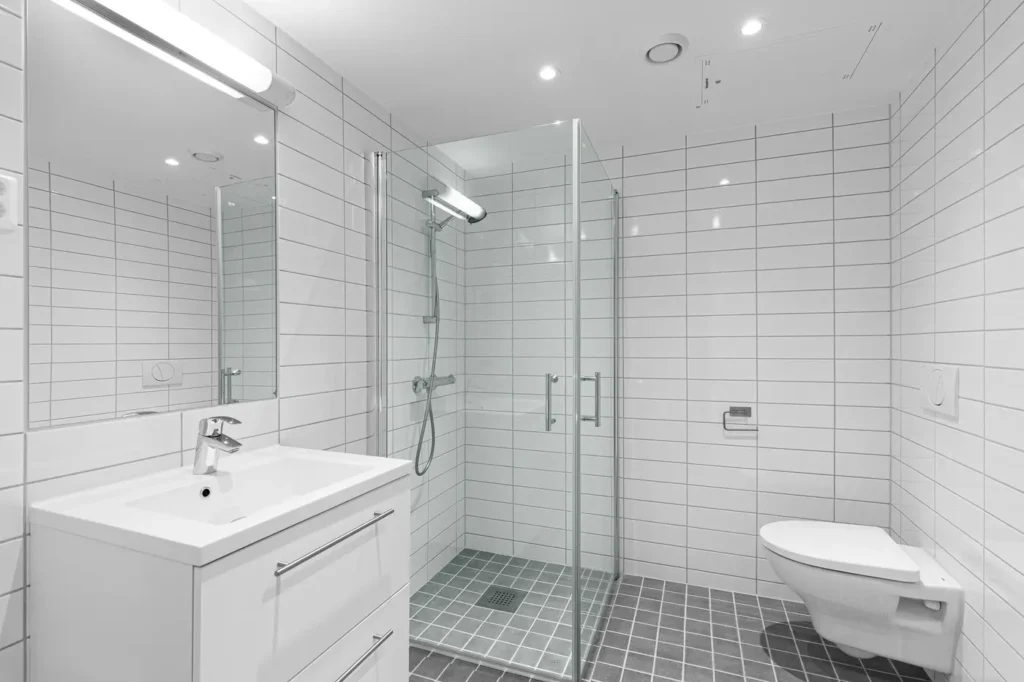 Burlington bathroom with framed glass shower door, chrome handheld showerhead, tiled shower pan, wall-mounted toilet, and vanity