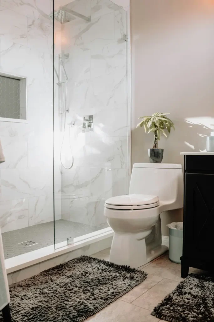 Marble-tiled glass shower enclosure with rain showerhead after a tub-to-shower conversion, next to a dark vanity