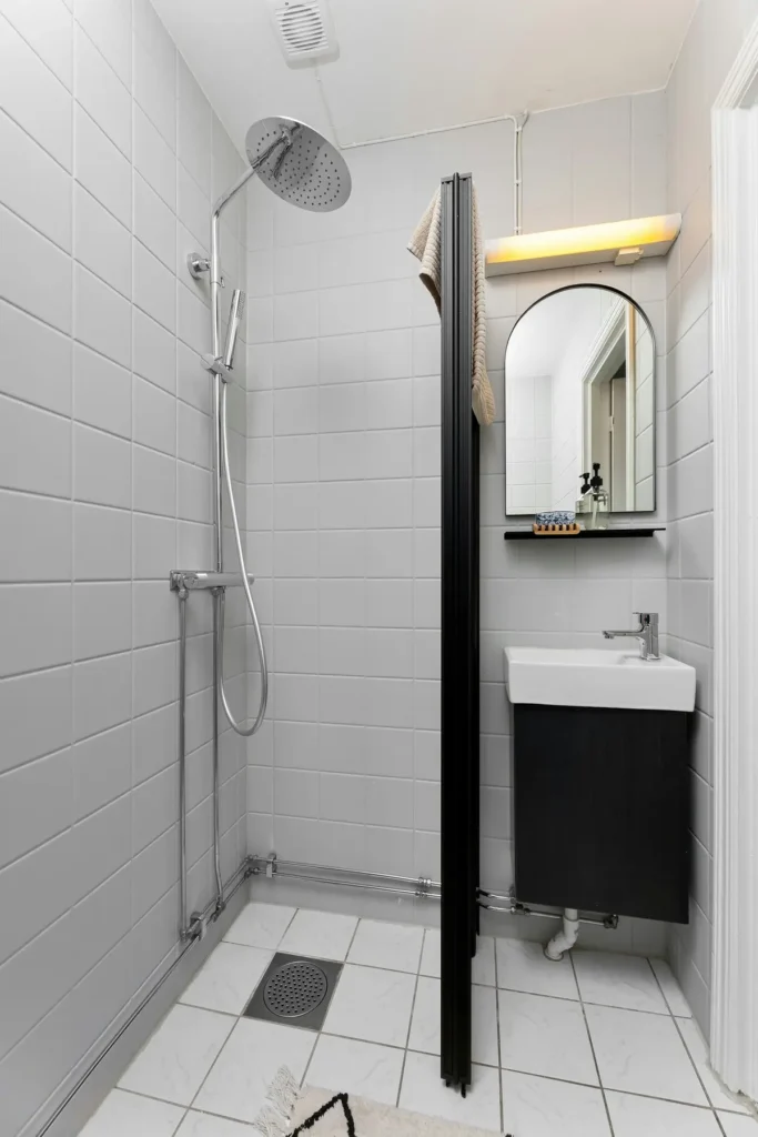 Open walk-in shower with rain showerhead, handheld sprayer, glass divider panel, and floor drain in an Alton Village, Burlington bathroom