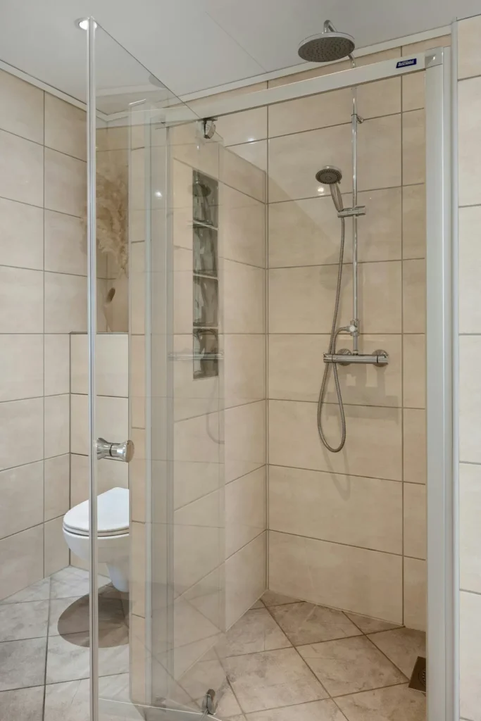Corner glass shower enclosure with a built-in tile niche, rain showerhead, and handheld sprayer