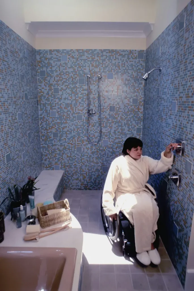 Person using a wheelchair inside a curb less, roll-in tiled shower with a flush entry floor